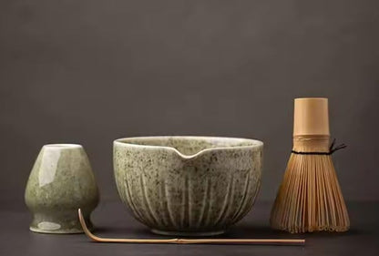 Three ceramic items including a bowl, cup, and whisk on a dark background